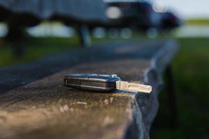 Autoschlüssel liegt auf einer Bank, im Hintergrund ist ein Fahrzeug zu sehen.